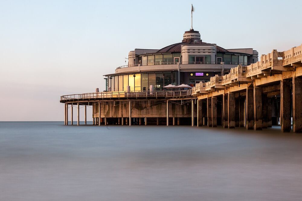 De verlichte Pier van Blankenberge boven het water in de avondschemering